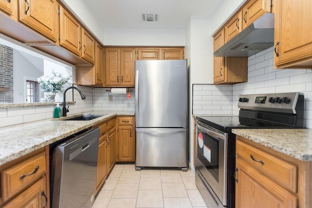 kitchen with light tile patterned flooring, sink, light stone counters, appliances with stainless steel finishes, and backsplash