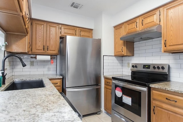 kitchen featuring light tile patterned flooring, sink, appliances with stainless steel finishes, light stone countertops, and decorative backsplash