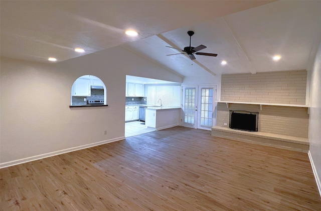 unfurnished living room with sink, a fireplace, ceiling fan, and light wood-type flooring