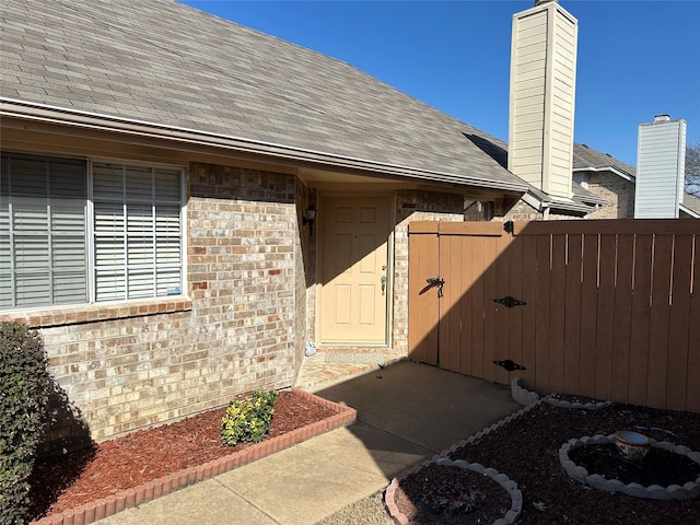 entrance to property featuring roof with shingles, a gate, fence, and brick siding