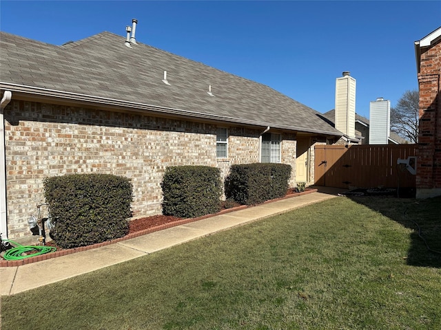 rear view of house featuring a shingled roof, fence, a lawn, and brick siding