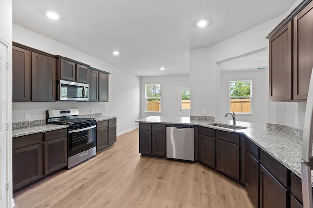 kitchen featuring sink, light stone counters, dark brown cabinetry, stainless steel appliances, and light hardwood / wood-style flooring