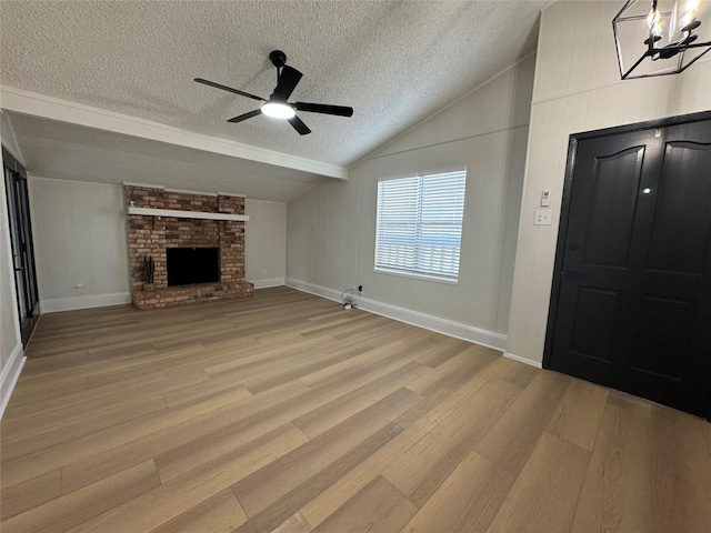 unfurnished living room with vaulted ceiling, a brick fireplace, a textured ceiling, and light hardwood / wood-style flooring