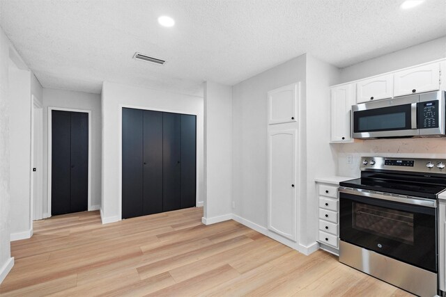 kitchen featuring appliances with stainless steel finishes, sink, white cabinets, light hardwood / wood-style floors, and a textured ceiling