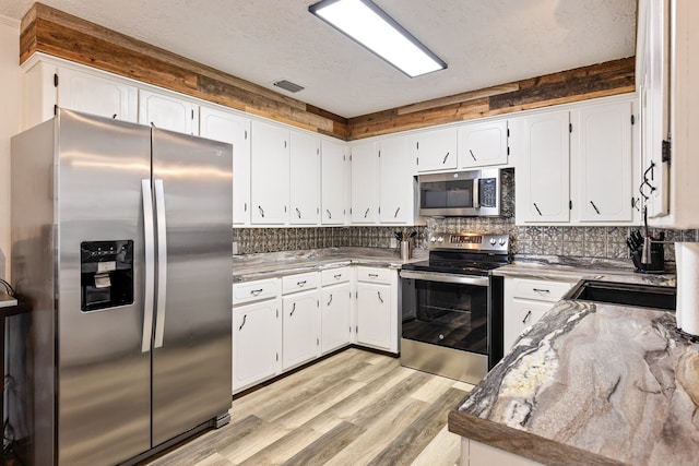 kitchen featuring white cabinetry, backsplash, light hardwood / wood-style floors, and appliances with stainless steel finishes