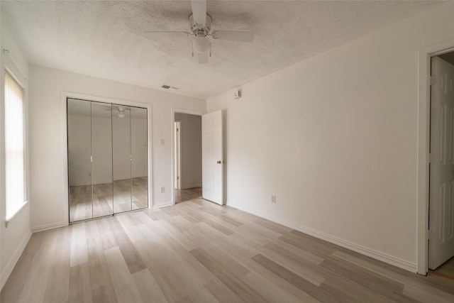 unfurnished bedroom featuring multiple windows, light hardwood / wood-style floors, and a textured ceiling