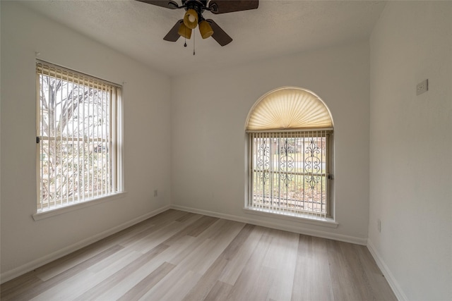 spare room with a textured ceiling, a wealth of natural light, ceiling fan, and light wood-type flooring