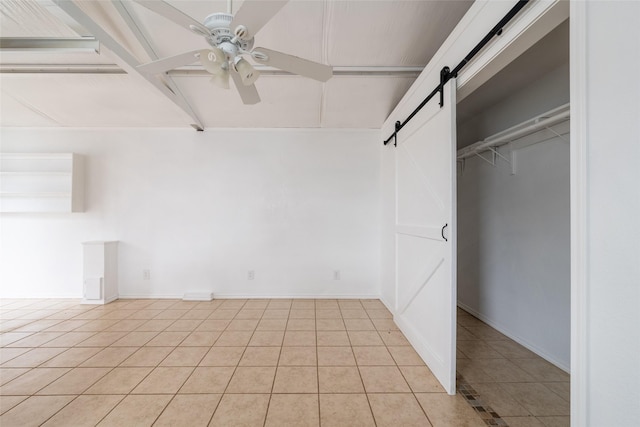 unfurnished bedroom featuring ceiling fan, a barn door, a closet, and light tile patterned floors