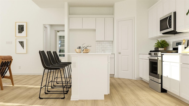 kitchen with a kitchen island, tasteful backsplash, white cabinets, stainless steel appliances, and light wood-type flooring