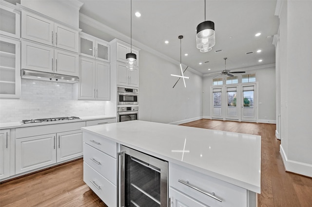 kitchen with white cabinetry, decorative light fixtures, stainless steel appliances, and beverage cooler