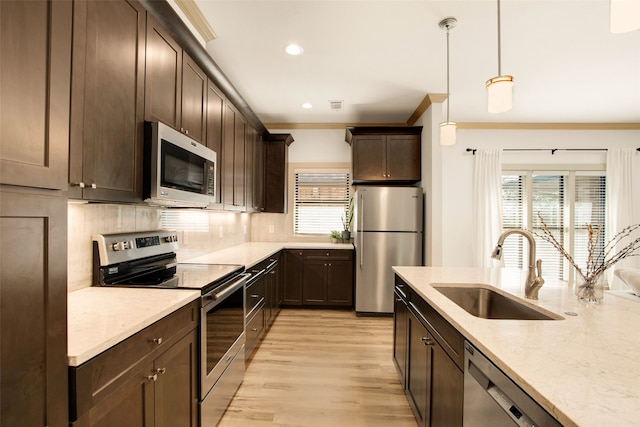 kitchen with appliances with stainless steel finishes, pendant lighting, sink, light stone counters, and crown molding