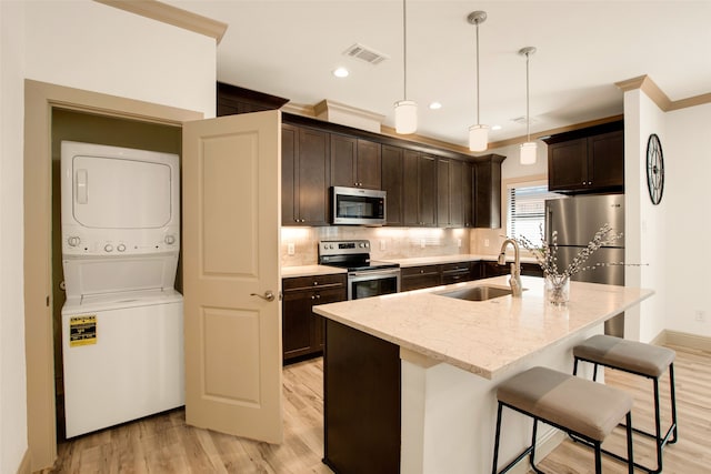 kitchen with stacked washer and dryer, sink, decorative light fixtures, an island with sink, and stainless steel appliances