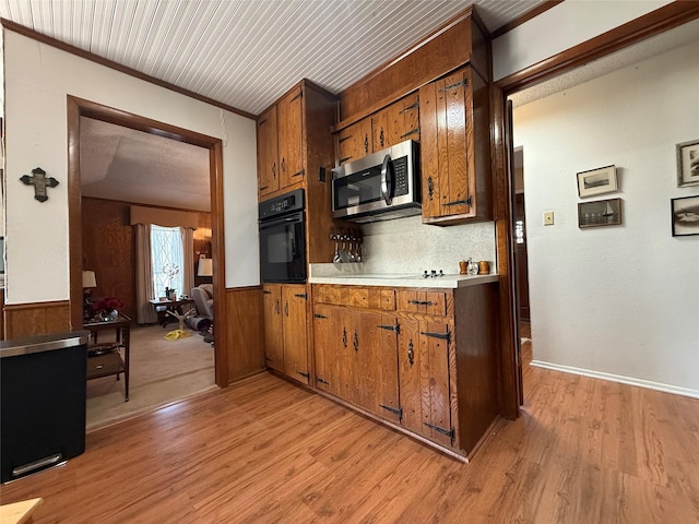 kitchen with wood walls, crown molding, light hardwood / wood-style floors, decorative backsplash, and black appliances