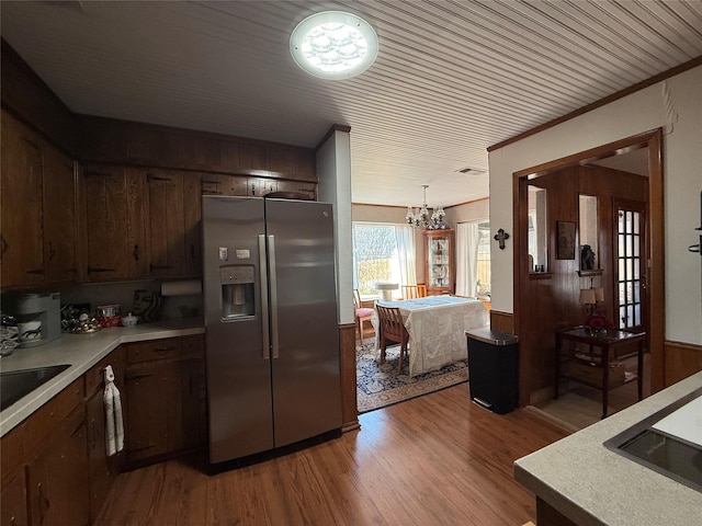 kitchen with pendant lighting, wooden walls, crown molding, light hardwood / wood-style floors, and stainless steel refrigerator with ice dispenser