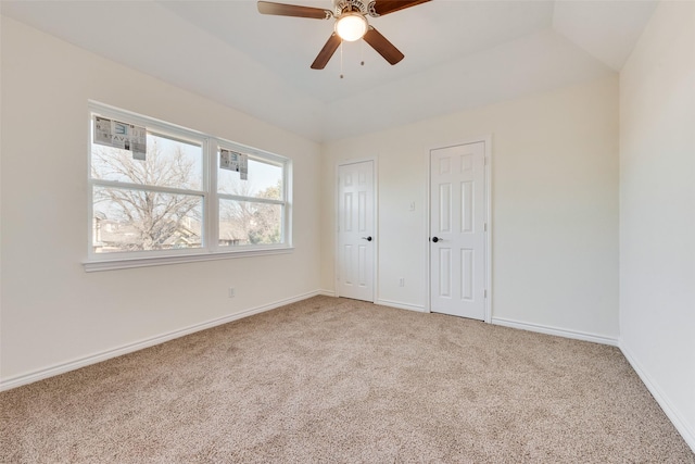 unfurnished bedroom with vaulted ceiling, multiple closets, a raised ceiling, carpet floors, and ceiling fan