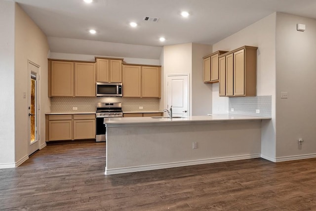 kitchen featuring sink, appliances with stainless steel finishes, dark hardwood / wood-style flooring, kitchen peninsula, and backsplash