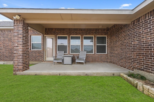 doorway to property with a patio area, a lawn, and brick siding