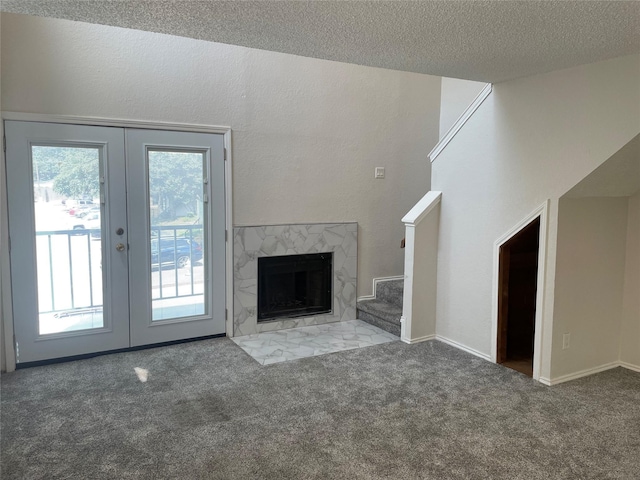 unfurnished living room with a premium fireplace, dark carpet, french doors, and a textured ceiling