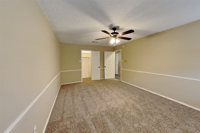 unfurnished bedroom featuring a spacious closet, a textured ceiling, carpet floors, a closet, and ceiling fan