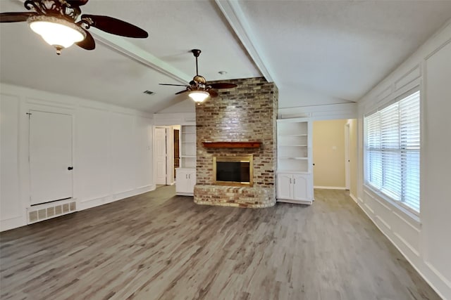 unfurnished living room featuring lofted ceiling with beams, a fireplace, built in shelves, and light hardwood / wood-style floors