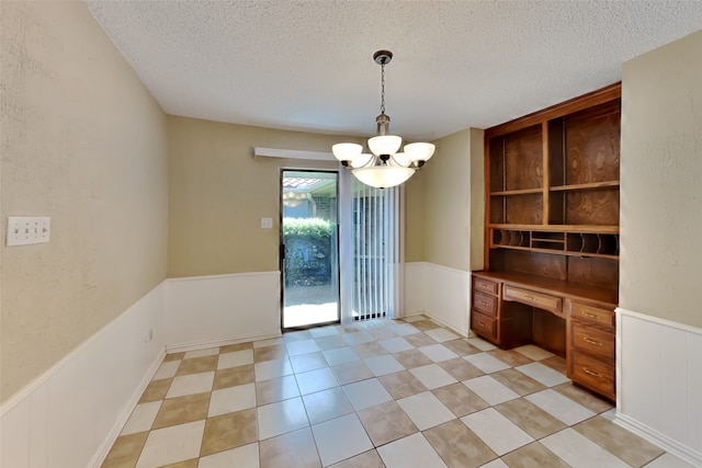 unfurnished dining area featuring a chandelier, built in desk, and a textured ceiling