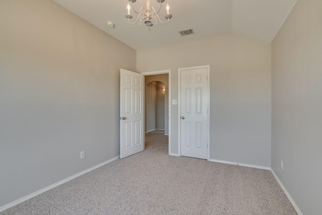 carpeted spare room with an inviting chandelier and vaulted ceiling