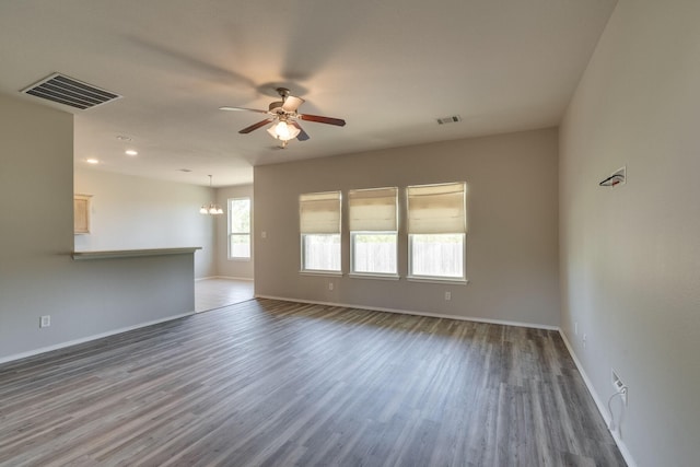 empty room with ceiling fan with notable chandelier and dark wood-type flooring