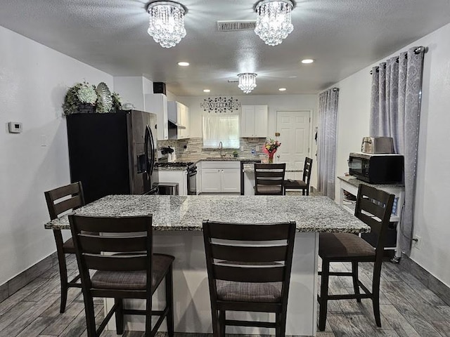 kitchen featuring white cabinetry, a kitchen bar, a chandelier, and black appliances