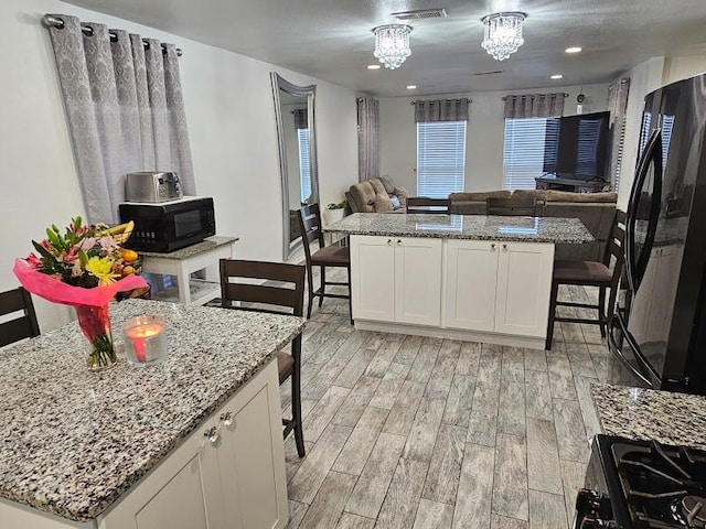 kitchen featuring white cabinetry, a breakfast bar, a center island, and black appliances