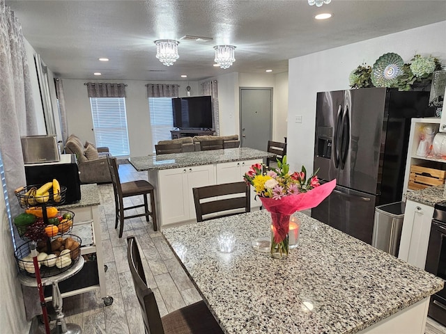 kitchen with stainless steel refrigerator with ice dispenser, a breakfast bar area, a center island, light stone countertops, and white cabinets