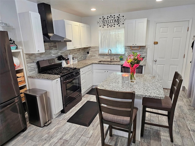 kitchen with a kitchen island, white cabinetry, sink, stainless steel appliances, and wall chimney exhaust hood