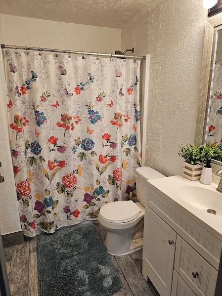 bathroom with hardwood / wood-style floors, vanity, walk in shower, toilet, and a textured ceiling