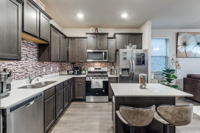 kitchen featuring sink, a breakfast bar area, backsplash, stainless steel appliances, and light hardwood / wood-style flooring