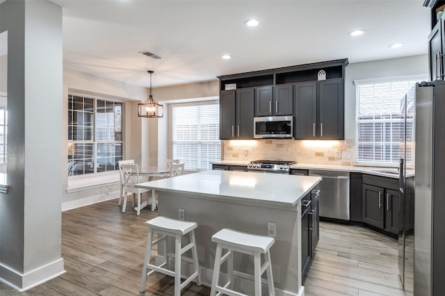 kitchen with tasteful backsplash, hanging light fixtures, a center island, stainless steel appliances, and light wood-type flooring