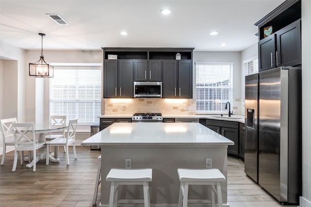 kitchen with sink, a breakfast bar, stainless steel appliances, a center island, and decorative light fixtures