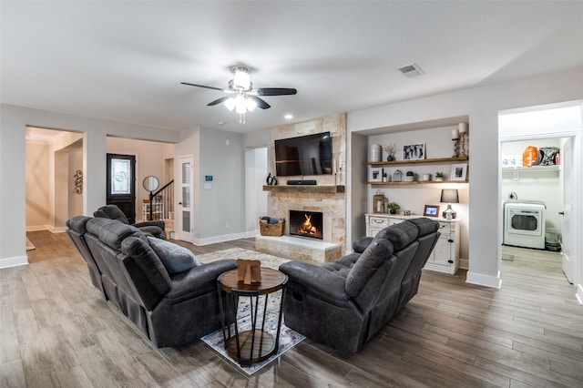 living room with ceiling fan, washer / clothes dryer, a stone fireplace, and light hardwood / wood-style flooring