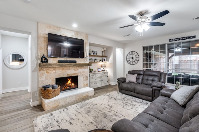 living room featuring ceiling fan, a fireplace, and light wood-type flooring