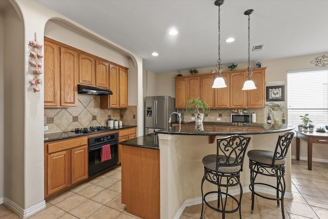 kitchen featuring light tile patterned flooring, appliances with stainless steel finishes, an island with sink, pendant lighting, and dark stone counters