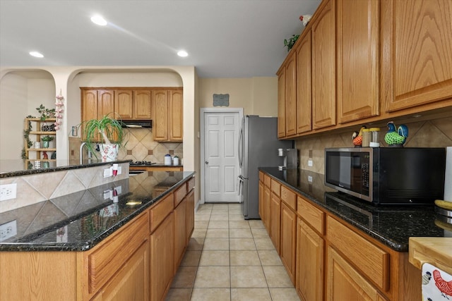 kitchen with dark stone countertops, light tile patterned floors, decorative backsplash, and stainless steel refrigerator