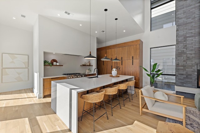 kitchen with decorative light fixtures, a kitchen bar, a large island with sink, a high ceiling, and light wood-type flooring