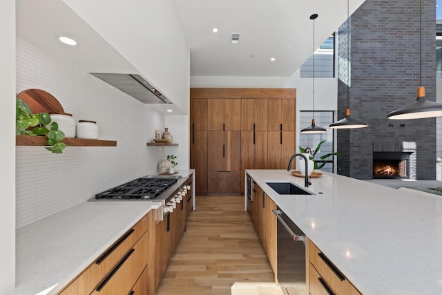 kitchen with sink, hanging light fixtures, light hardwood / wood-style floors, stainless steel appliances, and a brick fireplace