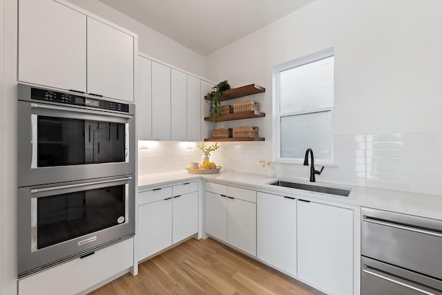 kitchen with sink, white cabinetry, tasteful backsplash, light hardwood / wood-style flooring, and stainless steel double oven