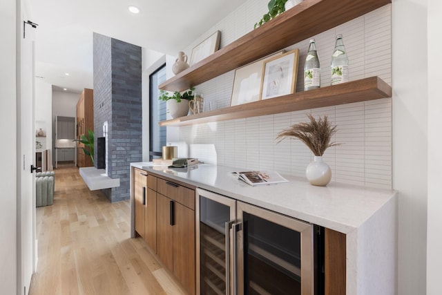 bar with wine cooler, backsplash, a large fireplace, and light wood-type flooring