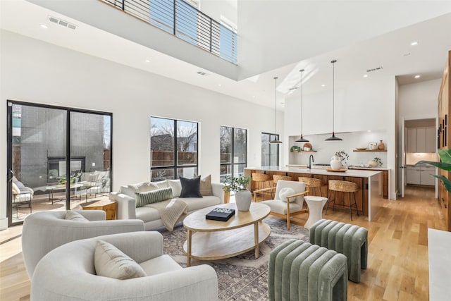 living room with a high ceiling, sink, and light hardwood / wood-style flooring