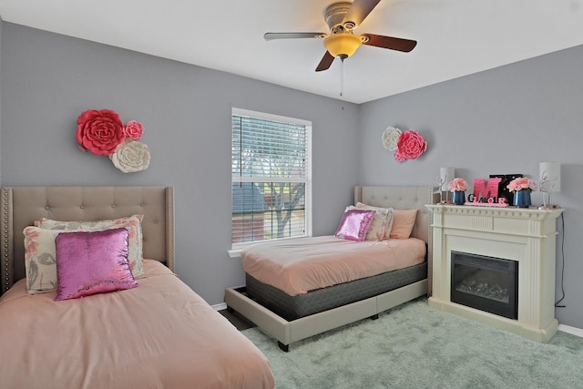 carpeted bedroom with a ceiling fan, a glass covered fireplace, and baseboards