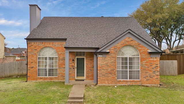 view of front of house featuring brick siding, a chimney, a front yard, and fence