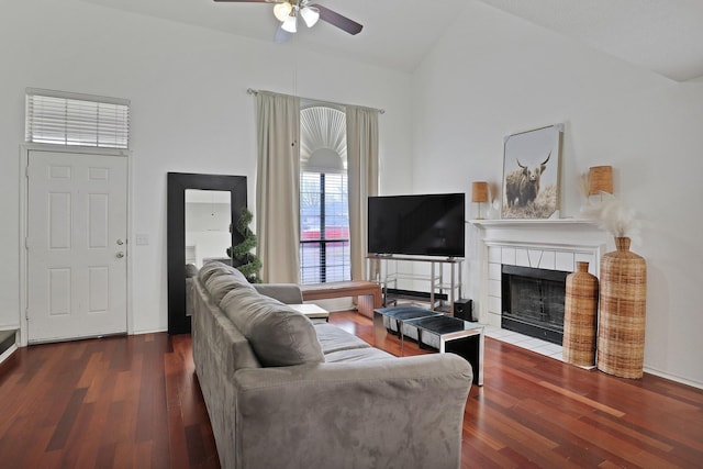 living room with a tiled fireplace, wood-type flooring, vaulted ceiling, and ceiling fan