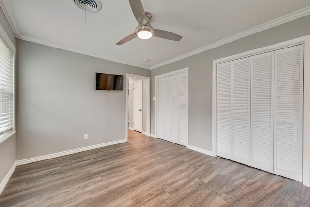 unfurnished bedroom featuring multiple closets, ornamental molding, ceiling fan, and light hardwood / wood-style flooring