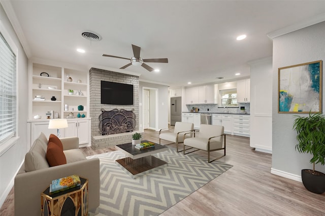 living room with ceiling fan, ornamental molding, a fireplace, and light hardwood / wood-style floors