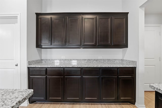 kitchen featuring light stone countertops, dark brown cabinets, and light wood-type flooring